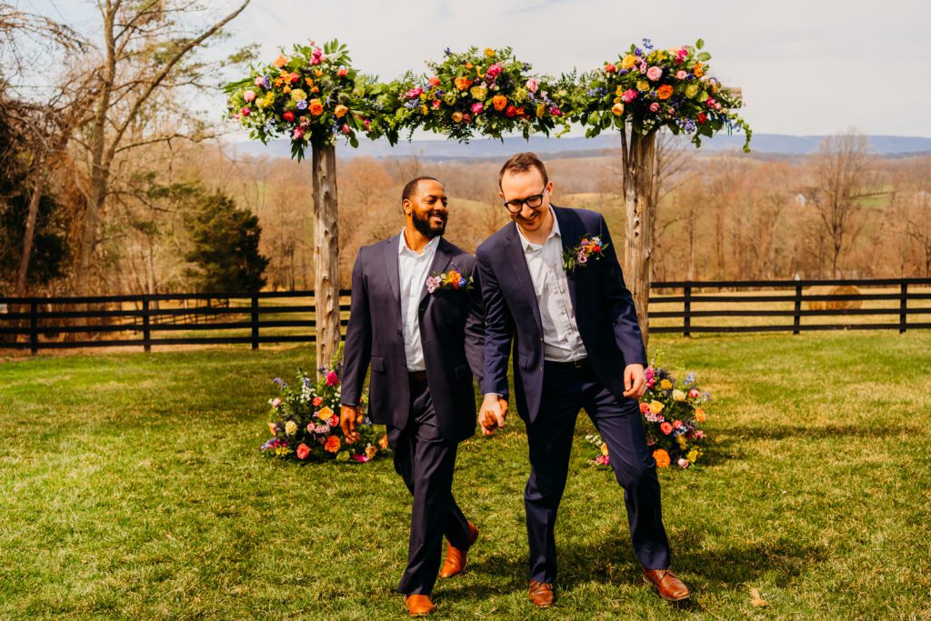 elopement couple walking hand in hand away from their rainbow floral arch after wedding