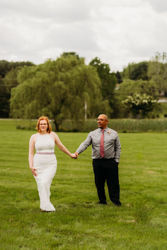wedding couple holding hands distant from each other in field