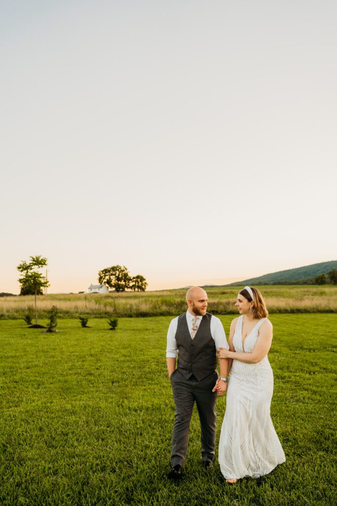 bride and groom holding ands walking in field in winchester va