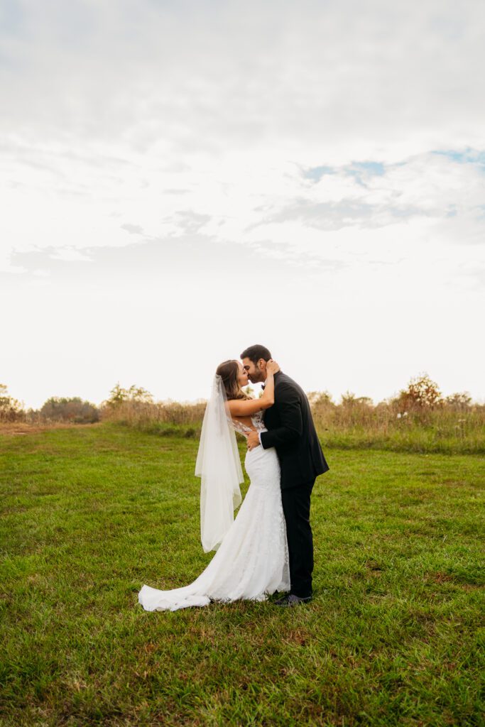 Bride in white dress kissing groom in a field