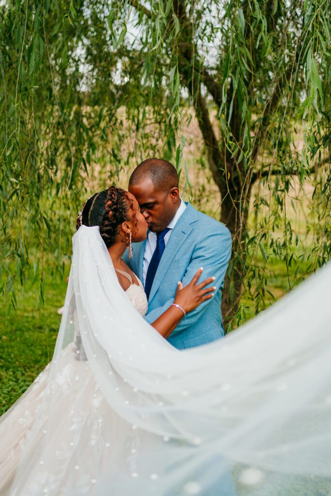 willow-tree-elopement-romantic-kiss-virginia.jpg Bride and groom share a kiss beneath a willow tree, her pearl-dotted veil flowing in the breeze