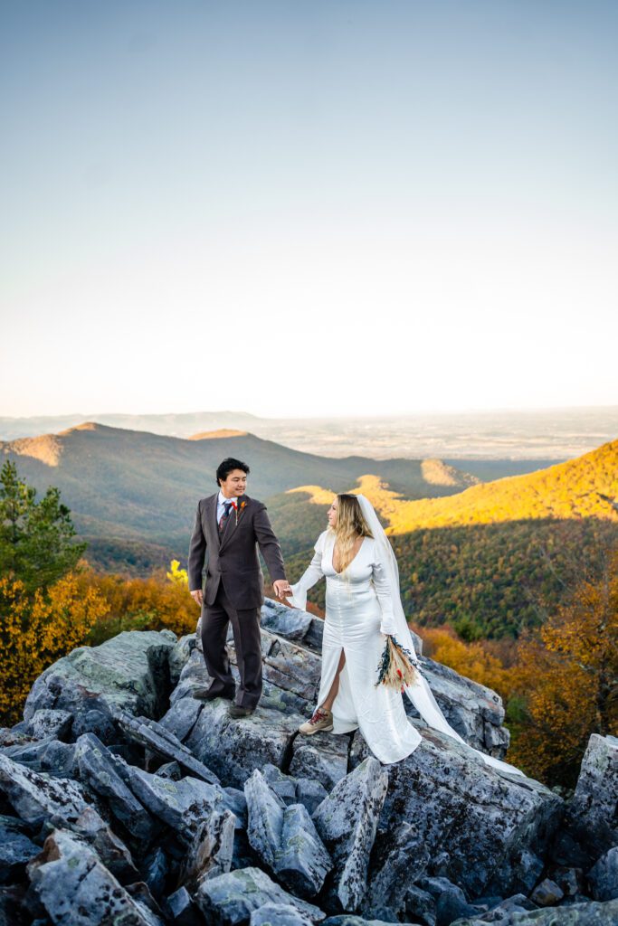 adventure-elopement-shenandoah-fall-hike.jpg Bride and groom explore rocky terrain at golden hour in Shenandoah Valley with fall colors in the background