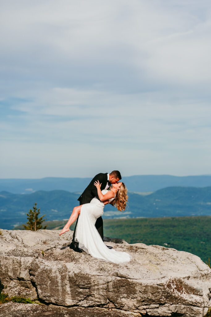 Groom dipping bride for a kiss on a rocky overlook during their adventurous mountaintop elopement