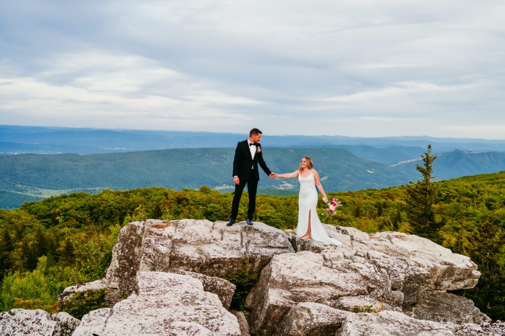 Bride and groom walking hand in hand along a rocky ledge during their scenic mountain elopement