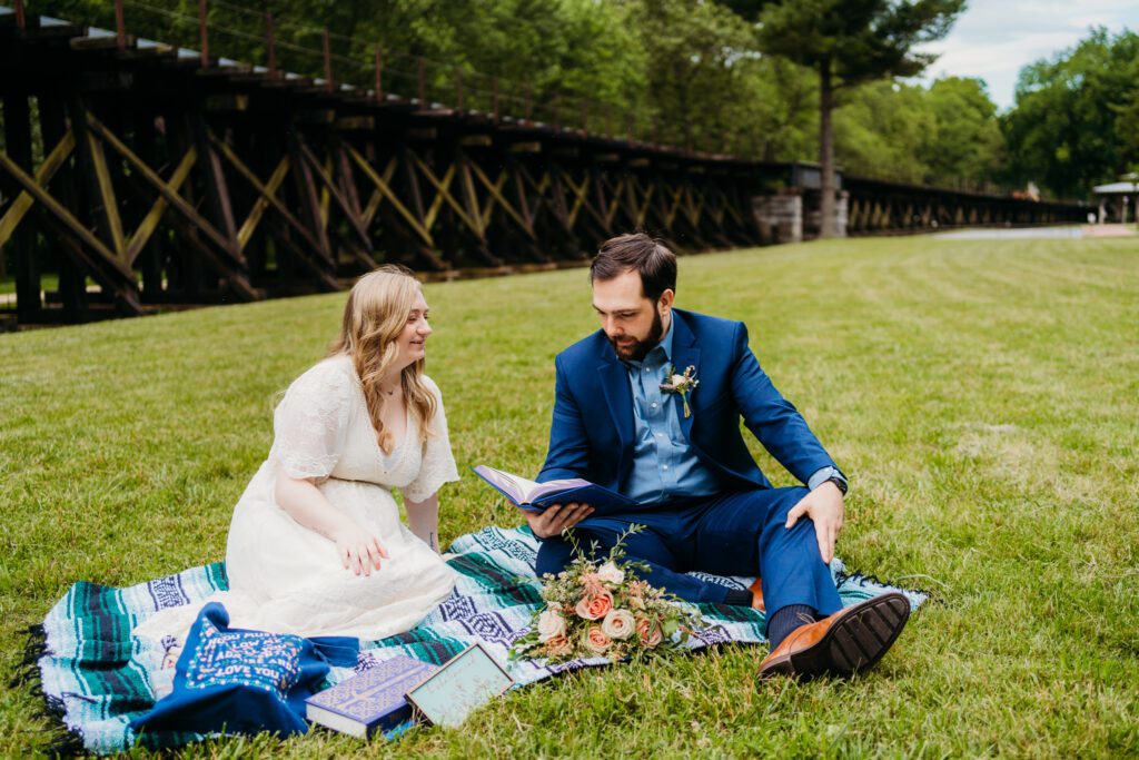 Bride and groom sit on a blanket surrounded by books and florals during a cozy, picnic-style West Virginia elopement.