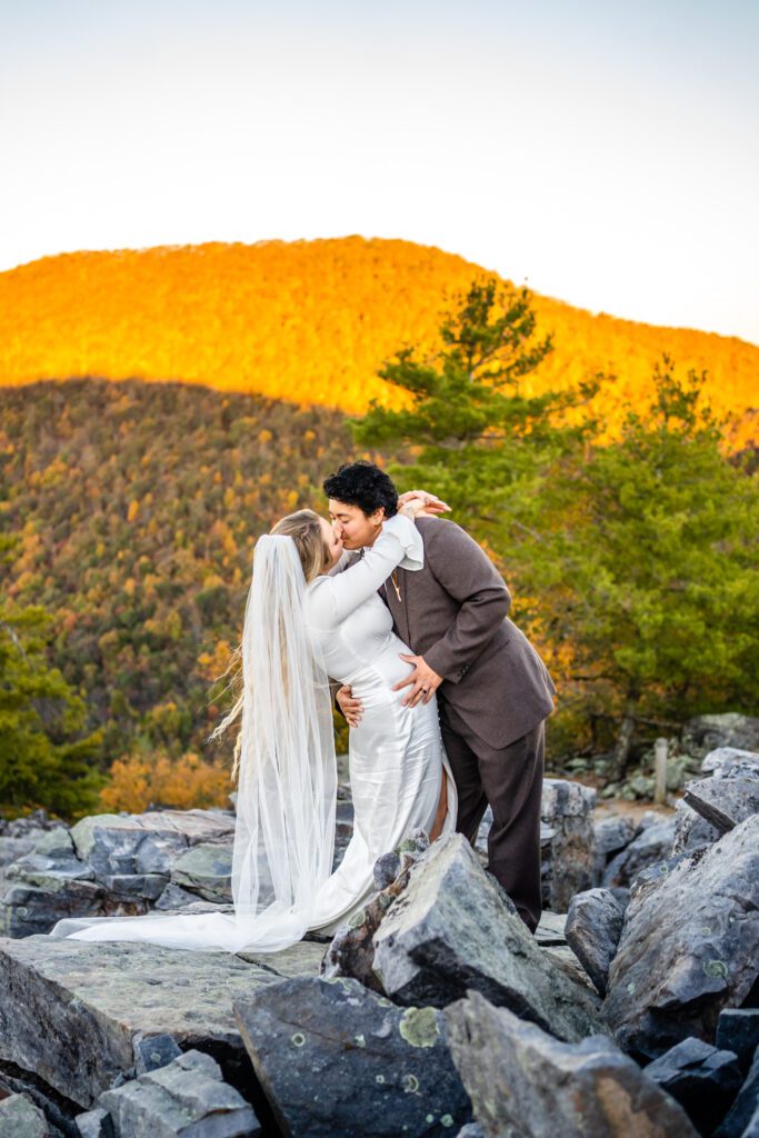 Bride and groom sharing a kiss at sunset with glowing Blue Ridge Mountains behind them in Shenandoah National Park.
