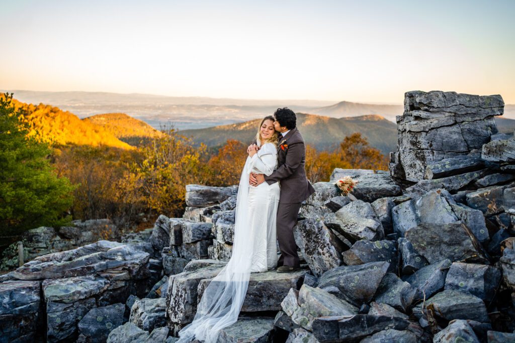Groom hugging bride from behind on mountaintop during romantic fall Shenandoah elopement