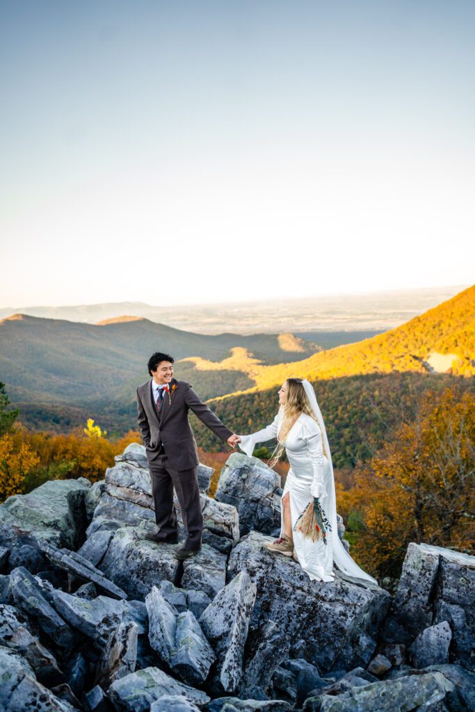 Adventurous couple walking hand in hand on rocky trail with panoramic views of Shenandoah Valley.