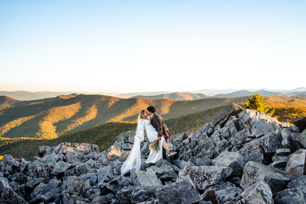 ride in satin gown and hiking boots during sunrise elopement on the rocky cliffs of Shenandoah National Park.