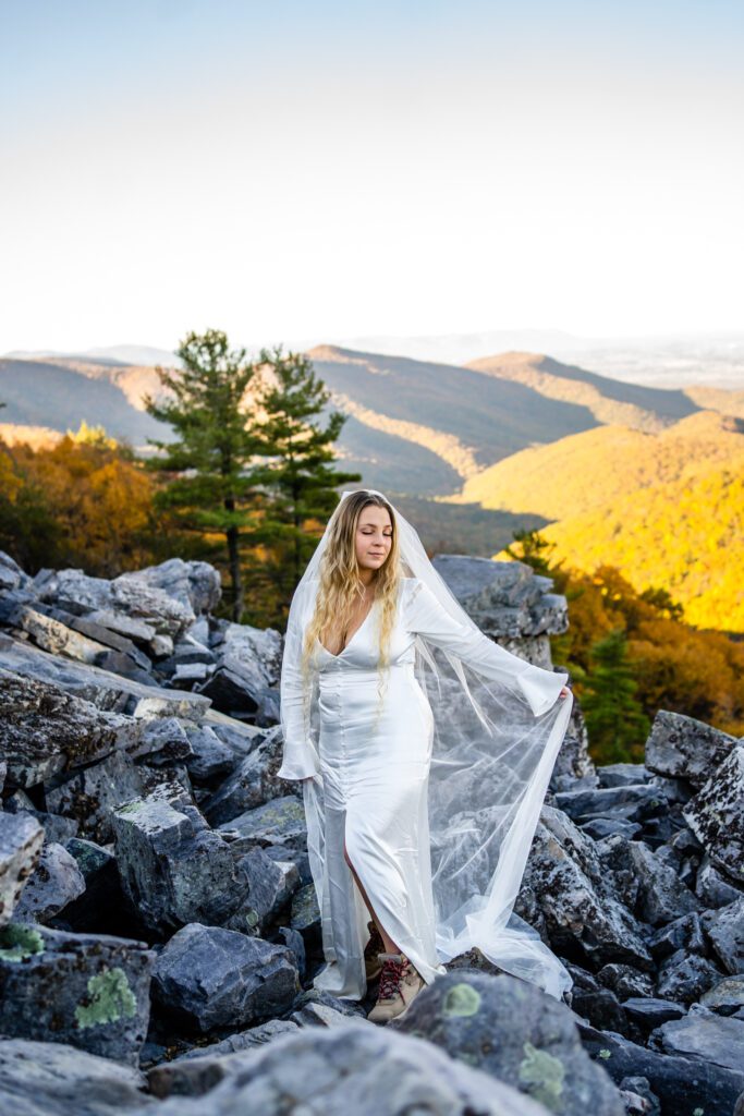 Bride’s veil blowing in the wind as couple embraces on a scenic overlook in Shenandoah during fall.