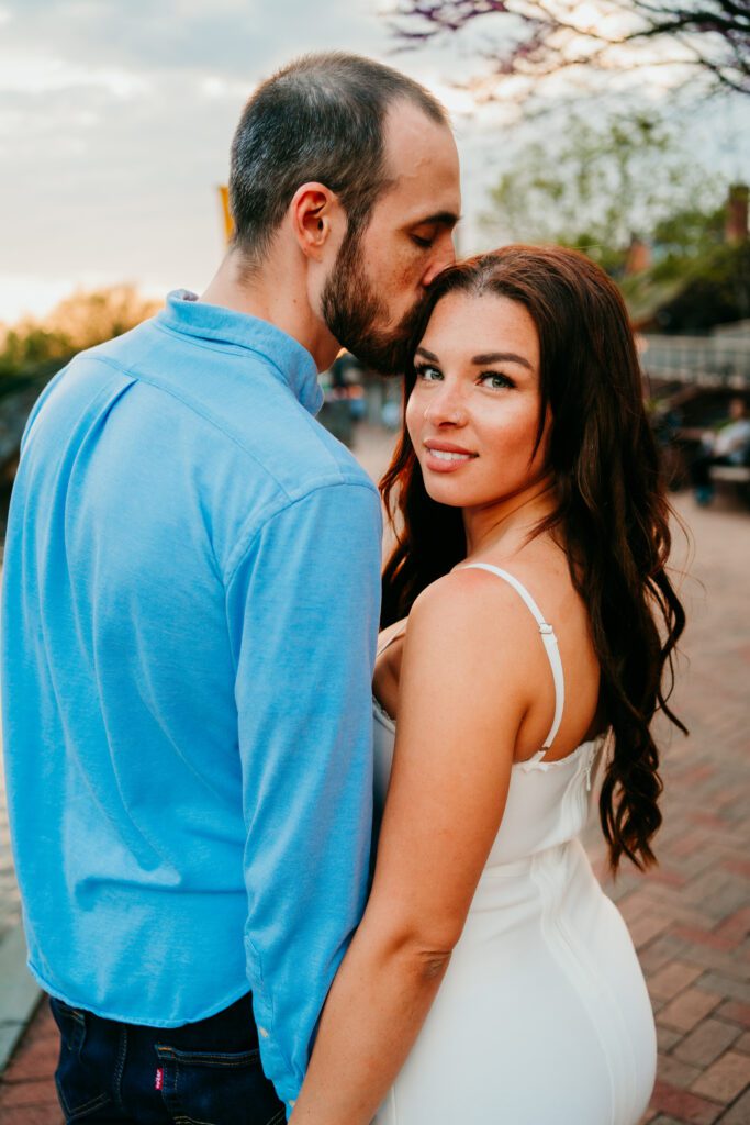 Groom kisses bride’s forehead during their Carroll Creek Park engagement session in Frederick MD